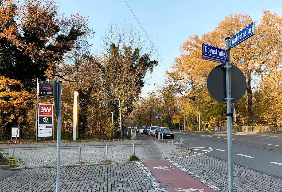 Straßenszene an einer Kreuzung mit einem Straßenschild, das die Goyastraße und die Waldstraße ausweist. Im Vordergrund verläuft ein Radweg, daneben stehen geparkte Autos entlang der Straße. Bäume mit herbstlich gelb gefärbten Blättern säumen den Straßenrand unter klarem Himmel.