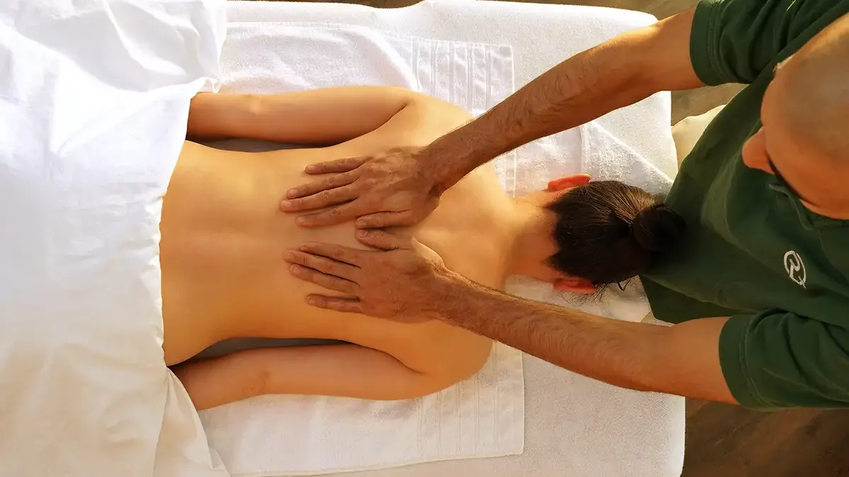 Thai-Massage: Therapeutin dehnt Schulter und Nacken einer Kundin