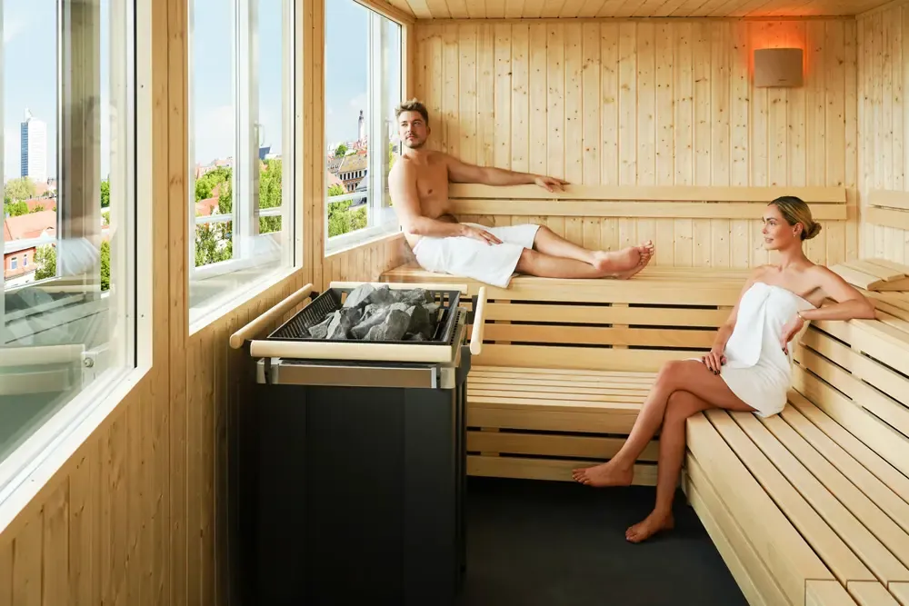 Paar in der Indoor-Sauna der LOUNGE-Etage am Panoramafenster mit Blick über Leipzig
