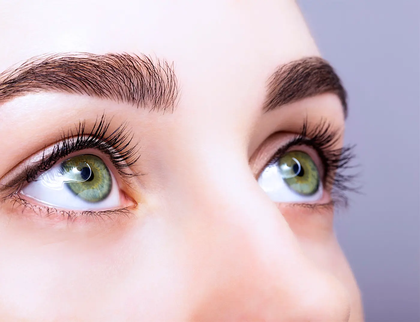 Frau mit grünen Augen schaut nach oben nach einem Wimpern- und Augenbrauenlifting