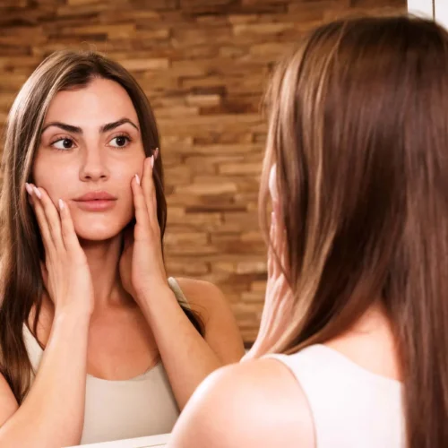 Frau nach Kosmetikbehandlung bei Relax Plus schaut sich zufrieden im Spiegel an