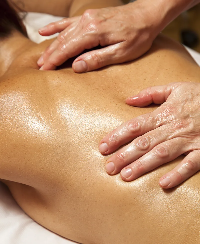 Nahaufnahme einer entspannenden Massagebehandlung mit geölter Haut und sanftem Handdruck auf dem Rücken einer liegenden Person.