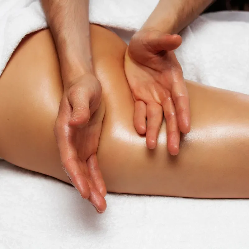 Sanfte manuelle Lymphdrainage an einem Bein, bei der ein Therapeut mit beiden Händen gleitende Bewegungen auf der geölten Haut ausführt.