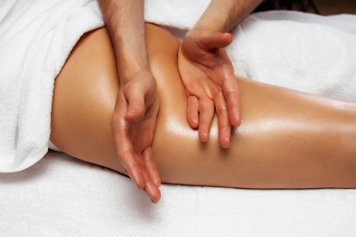 Sanfte manuelle Lymphdrainage an einem Bein, bei der ein Therapeut mit beiden Händen gleitende Bewegungen auf der geölten Haut ausführt.