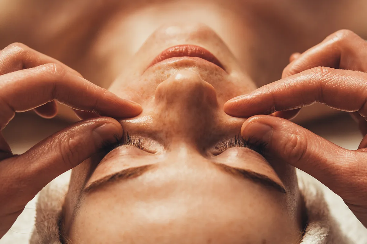 Sanfte Lymphdrainage im Gesicht mit zwei Händen, die die Haut unterhalb der Augen massieren.