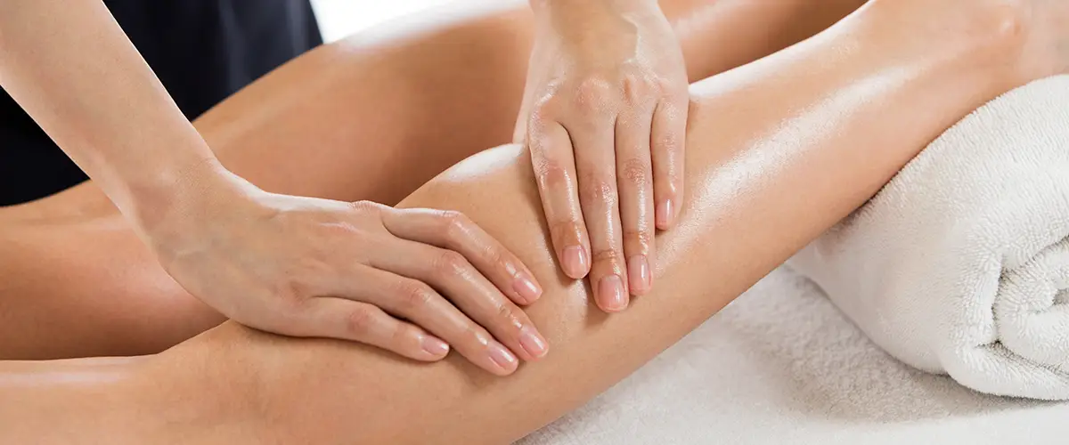 Hände massieren den Unterschenkel einer Person, die auf einer Liege liegt.