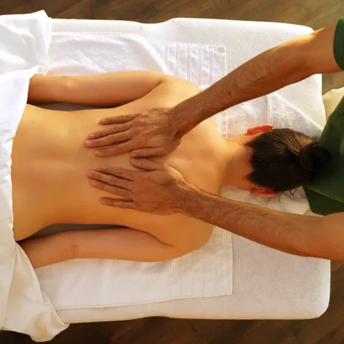 Rückenmassage einer liegenden Frau mit beiden Händen, Teil der Thai-Massage-Behandlung.