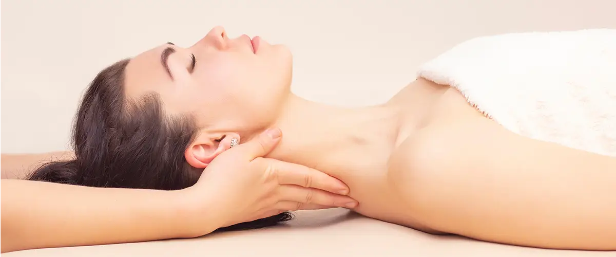 Frau liegt entspannt auf einer Massagebank, während eine Hand sanft ihren Nacken massiert.