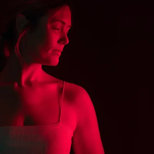 Frau steht vor einem LED-Rotlichtpanel in einem dunklen Raum und genießt eine Lichttherapie.