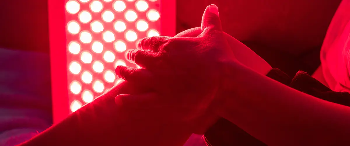 Hände massieren ein Bein unter der Bestrahlung eines LED-Rotlichtpanels.