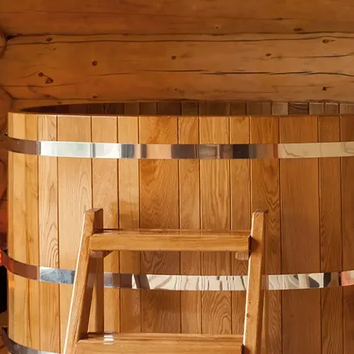 Rundes Holz-Tauchbecken mit Metallringen in einer Holzhütte, daneben ein Waschbecken.