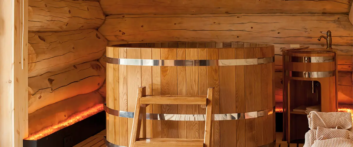 Rundes Holz-Tauchbecken mit Metallringen in einer Holzhütte, daneben ein Waschbecken.