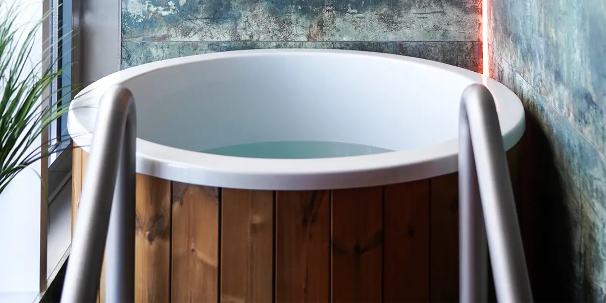 Rundes Tauchbecken aus Holz mit weißem Innenrand und Wasserfüllung, Metallgeländer und dekorative Wand im Hintergrund.