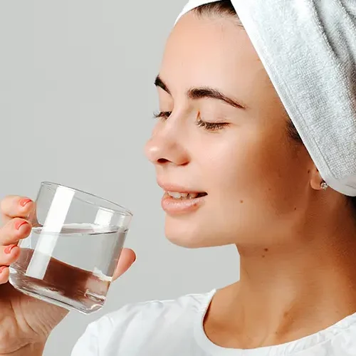 Frau mit Handtuchturban trinkt nach dem Saunagang ein Glas Wasser und genießt die Erholung.