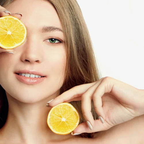 Frau hält sich 2 aufgeschnittene Orange vor hals und Gesicht