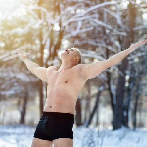 Oberkörperfreier Mann mit ausgestreckten Armen in der kalten Natur