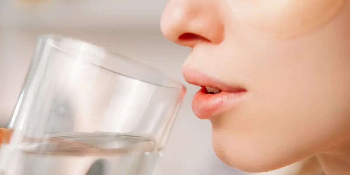 Nahaufnahme einer Frau mit Augenpads, die kurz davor ist, ein Glas Wasser nach der Sauna oder Massage zu trinken.